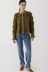 Saco tejido de punto color verde oliva, con diseño de calados y esferas en relieve en la parte superior y mangas. Presenta cierre frontal con botones, cuello redondo y puños acampanados con detalle de borde en contraste.