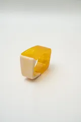 Anillo de resina con diseño geométrico cuadrado, combinando una sección en color amarillo translúcido y otra en color crema con efecto marmolado.