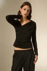 Top de manga larga color negro, con cuello en V y diseño drapeado en el frente. Confeccionado en tejido ajustado al cuerpo.