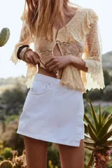 Falda pantalón corta de tiro alto color blanco, con bolsillos delanteros y traseros. Cierre frontal cruzado con cremallera oculta y botón metálico.