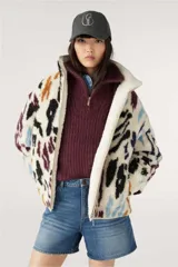 Campera bomber reversible con un lado de corderito estampado con manchas abstractas en tonos negro, marrón, azul y violeta sobre fondo blanco, y del otro lado liso en tono crudo.