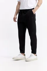 Pantalón de jogging negro de algodón y poliéster, con puños ajustados en los tobillos, cintura elástica con cordón y costuras verticales marcadas en el frente.