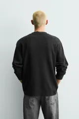 Camiseta de corte relajado confeccionada en tejido de algodón con textura waffle. Presenta cuello redondo con cierre frontal de botonadura y manga larga.