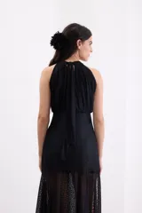 Vestido largo de encaje negro, con escote halter y falda translúcida con tajo delantero.