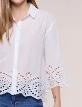 Camisa de calce holgado color blanco, confeccionada en tejido liviano de algodón, con cuello camisero clásico, mangas tres cuartos y terminación en puños y ruedo con diseño de bordado broderie calado y festoneado.