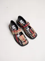 Zapatos tipo guillermina con punta cuadrada, confeccionados en lona resistente con estampado de cuadros escoceses en tonos beige, rojo y negro. Presentan una correa ajustable con hebilla metálica color bronce y una suela con taco de 4 cm.