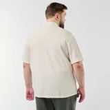 Camisa de manga corta en color blanco, confeccionada en tejido de punto con textura geométrica. Presenta cuello camisero abierto y cierre frontal con botones marrones de efecto carey.