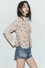 Camisa entallada de manga larga con cuello solapa, cierre frontal de botones y detalle de volantes en el delantero, confeccionada en tejido con estampado floral.