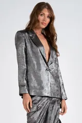 Blazer plateado de satén laminado, con cuello con solapa y abertura central con botón. Forro interno a tono.