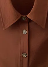 Vestido midi de color marrón, con diseño evasé, cuello camisero y cierre frontal con botones. Presenta un cinturón ajustable a la cintura y un diseño sin mangas con tirantes anchos.