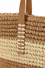 Bolso de playa tejido en rafia color beige con rayas horizontales negras y asas de cuero sintético marrón.