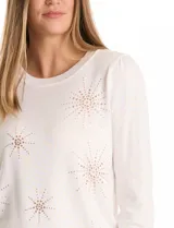 Buzo de punto liviano color blanco, con cuello redondo y mangas largas con frunce en la copa. Presenta apliques de strass en forma de destellos distribuidos en el frente. Cuenta con puños y cintura en tejido acanalado.