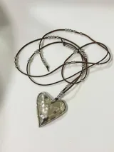Collar con tres dijes de corazón irregular hechos a mano en alpaca o bronce, con tiento de gamuza negro y cuentas plateadas. El largo del tiento permite darle varias vueltas o usarlo largo.