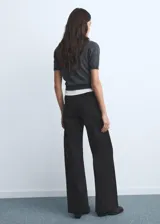 Jeans wide leg tiro alto de color negro, con cierre delantero de cremallera y botón, trabillas para cinturón y dos bolsillos de parche en la parte delantera.