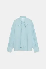 Camisa de rayas celestes y blancas de la colección ZW de Zara, con cuello redondo, lazada en el mismo tejido en el escote y mangas largas con puños anchos.