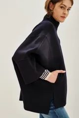 Tapado corto de paño en color azul marino, con cuello alto, cierre frontal de botones y mangas amplias de corte kimono. Presenta aberturas laterales en el ruedo y bolsillos frontales.