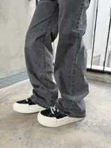 Pantalón de jean color negro lavado, de corte recto y tiro alto. Presenta detalles de tachas metálicas a lo largo de las costuras laterales superiores.