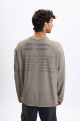 Remera de manga corta color verde oliva, confeccionada en tejido french terry, con estampado en la espalda que simula un cartel de gira de banda con fechas y lugares.