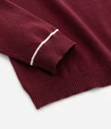 Suéter de punto en color bordó con corte slim, cuello polo y mangas largas. Presenta detalles de líneas blancas en contraste en el cuello y los puños, con acabado acanalado.