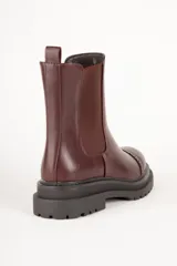 Bota Chelsea de cuero sintético color negro, con elástico lateral, puntera redondeada con detalle de perforaciones y suela track.