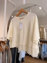 Remera oversize de algodón color marfil, con mangas cortas y detalle de terminación inferior con puntilla bordada.