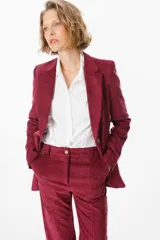 Blazer de corte clásico confeccionado en tela aterciopelada color bordó, con cuello solapa, cierre frontal con botones y bolsillos laterales tipo ojal.