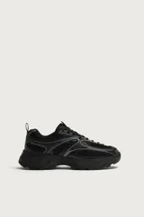 Zapatilla deportiva tipo running de color negro, confeccionada en una combinación de piezas de malla y material sintético. Presenta un diseño con cordonera curvada y una suela de volumen con diseño irregular.