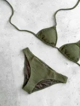 Bikini color verde militar con textura acanalada. El top es de triángulos movibles con almohadillas desmontables y se ata al cuello y espalda. El bottom es una vedetina ancha con laterales fijos.