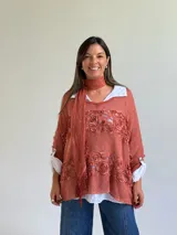 Sweater de punto color naranja con diseño holgado, que incorpora franjas horizontales de encaje con motivos florales. Presenta mangas tres cuartos con puños abotonados y se complementa con una bufanda del mismo tejido y color.