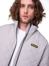 Campera puffer Caterpillar color gris claro, con cuello alto, cierre frontal completo y diseño acolchado con patrón chevron. Cuenta con parche del logo de la marca en el pecho.