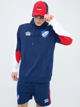 Canguro deportivo Umbro del Club Nacional de Football, modelo Nexo para hombre. Diseño en color azul marino con mangas rojas y detalles en celeste y blanco, capucha con cordón ajustable y bolsillo tipo canguro.