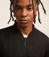 Campera bomber negra para hombre, confeccionada en poliéster con cierre frontal de cremallera, cuello, puños y dobladillo elásticos acanalados, y bolsillos laterales.
