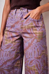 Jean wide leg de tiro alto en color lila, con un llamativo estampado de hojas grandes en tonos marrones sobre un sutil fondo de cuadros.