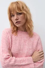 Sweater de punto con diseño de trenzas verticales, color rosa melange, de cuello redondo y manga larga con puños acanalados.