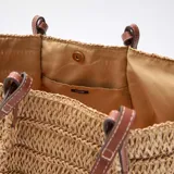 Capazo de paja color beige con asas largas de cuero marrón.