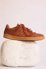 Zapatillas bajas color marrón con cordones y charms dorados.