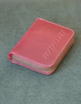 Billetera de cuero color salmón con cierre de cremallera y diseño de líneas verticales en relieve.