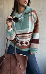 Sweater de tejido de punto con diseño a rayas horizontales y patrón geométrico en tonos verde, marrón y beige. Presenta cuello alto con cierre frontal, mangas largas abullonadas con puños ajustados y corte holgado.