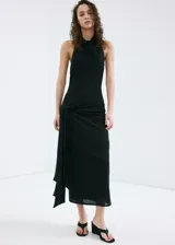 Vestido largo negro de corte slim, con cuello drapeado, sin mangas y detalle de fruncido lateral con caída de tela en la cadera.