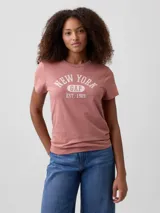 Remera de manga corta con cuello redondo, color rosado, con estampa frontal con texto New York Gap Est. 1969 en color blanco.