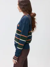 Sweater de punto cable con diseño a rayas horizontales en azul marino, verde y naranja. Presenta cuello redondo acanalado, puños y ruedo elásticos, y logo bordado en el pecho.