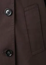 Chaqueta marrón de corte recto y diseño crop, confeccionada en mezcla de algodón y poliamida con forro interior de poliéster. Presenta cuello alto tipo embudo, doble botonadura frontal, manga larga y dos bolsillos laterales.