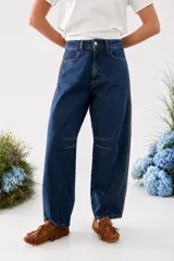Pantalón jean de corte barrel en azul oscuro con paneles laterales negros, diseño de tiro alto y costuras decorativas en las rodillas.
