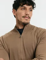 Cardigan de punto color marrón, con cuello alto y cierre frontal completo. Presenta mangas largas tipo ranglan y bolsillos laterales de ribete.