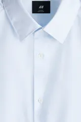 Camisa de corte entallado con cuello inglés, canesú en la espalda y mangas largas con puños ajustables. Presenta un diseño de rayas verticales finas y un bajo levemente redondeado.