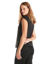 Blusa negra de punto elástico con caída fluida, cuello redondo y apliques de tachas doradas circulares en el cuello y los hombros. Tiene manga casquillo y ruedo redondeado.