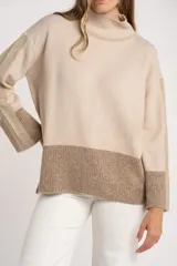 Sweater tipo polera de calce oversize, con diseño color block que combina tonos beige y marrón. Presenta cuello alto, mangas largas con puños acanalados y un panel inferior acanalado a juego.