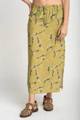 Falda midi color verde oliva con estampado de ramas en negro y blanco. Tiene corte evasé, cintura alta con cordón ajustable y abertura lateral.