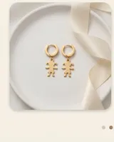 Aros tipo argolla con cierre a presión, de los cuales cuelga un dije con forma de silueta de niña, en acabado dorado.