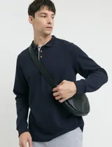 Remera de punto canalé francés, color azul marino, con cuello polo, manga larga y abotonadura frontal con botones de madera. Presenta detalles a contratono en la cartera y el interior del cuello.